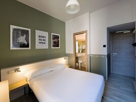 Hotelkamer met een bed, nachtkastje, wandlamp, ingelijste foto's en een zichtbare badkamer door een geopende deur.