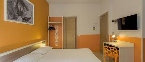 A hotel room with a bed, a desk, a chair, a wardrobe, and a TV.