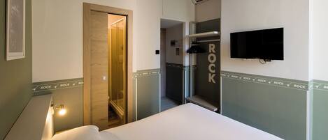Ein Hotelzimmer mit Bett, Wand-Fernseher, Duschbereich und einer Tür zu einem weiteren Raum.