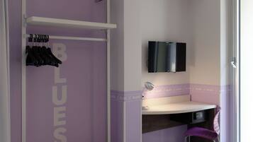 Ein Zimmer mit violettem Akzent an der Wand, einer Holzbank, einem Schreibtisch mit Stuhl und einem an der Wand befestigten Fernseher.
