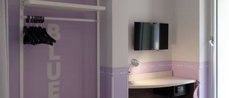 A room with a purple accent wall, a wooden bench, a desk with a chair, and a mounted TV.