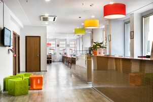 Een moderne hotellobby met een receptiebalie, zithoek en een gang naar de kamers.