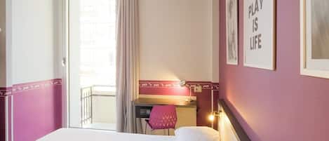 A hotel room with a bed, a desk, a chair, and a window with curtains.