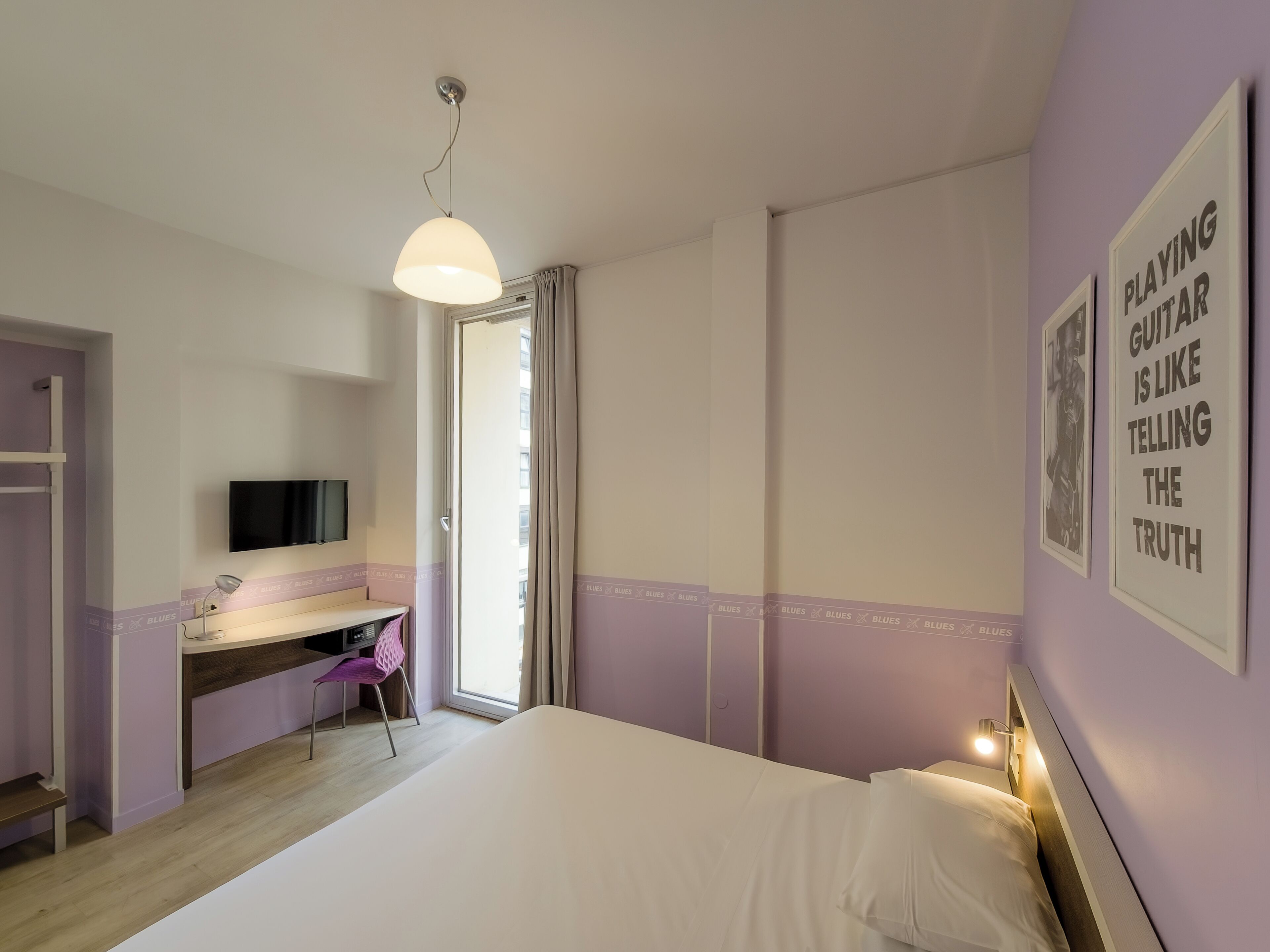 A bedroom with a bed, a desk, a chair, a TV, and a door leading to a balcony.