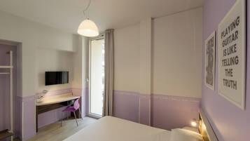 Una camera da letto con un letto, una scrivania, una sedia, una televisione e una porta che dà su un balcone.