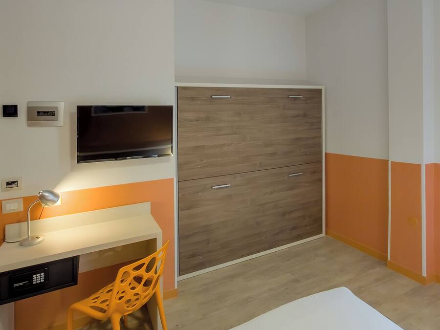 Una habitación moderna con un escritorio blanco, una silla naranja, un televisor y un armario.
