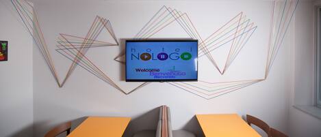 A hotel room with a modern geometric wall design, a flat-screen TV displaying 'hotel Nologo' and 'Welcome', and a yellow table with two chairs.