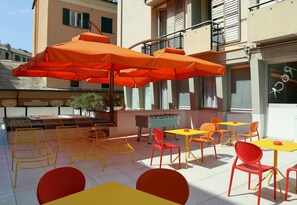An outdoor seating area with orange umbrellas, yellow and red chairs, and tables. - Sure Hotel by Best Western Nologo (Genoa)