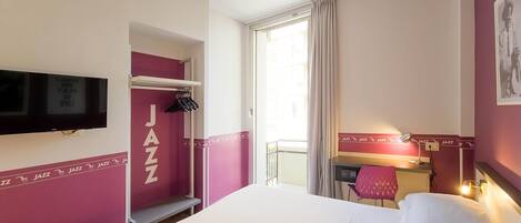 A hotel room with a bed, a desk with a chair, a television mounted on the wall, and a balcony with a view.