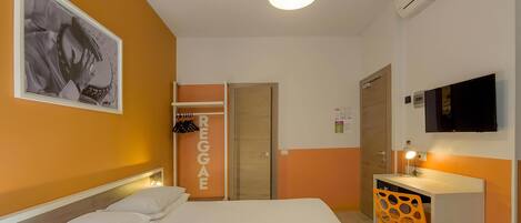 A hotel room with a bed, a desk, a chair, a wardrobe, and a television.