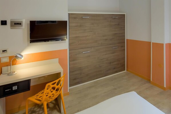 A room with a desk, chair, TV, wardrobe, and a small rug. - Sure Hotel by Best Western Nologo (Genoa)