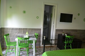 Een kamer met een bed, een tafel met stoelen, een televisie aan de muur en een deur naar een badkamer.