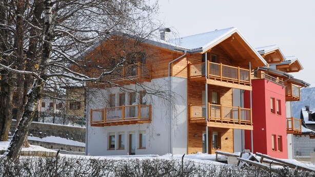 A multi-story building with a wooden balcony, a red section, and a snow-covered landscape. - Residence Marisol (Mezzana)