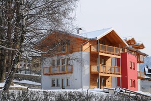 A multi-story building with a wooden balcony, a red section, and a snow-covered landscape. - Residence Marisol (Mezzana)