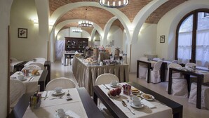 Comedor con mesas dispuestas para el desayuno, que cuenta con techo de ladrillo y ventanas de arco.