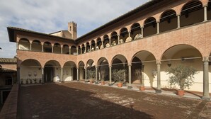 Un patio con un edificio de ladrillo que presenta paseos con arcos y una torre.