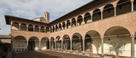 A courtyard with a brick building featuring arched walkways and a tower.