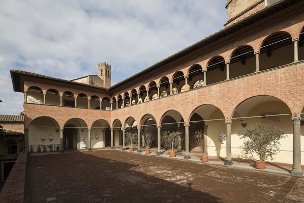 A courtyard with a brick building featuring arched walkways and a tower.