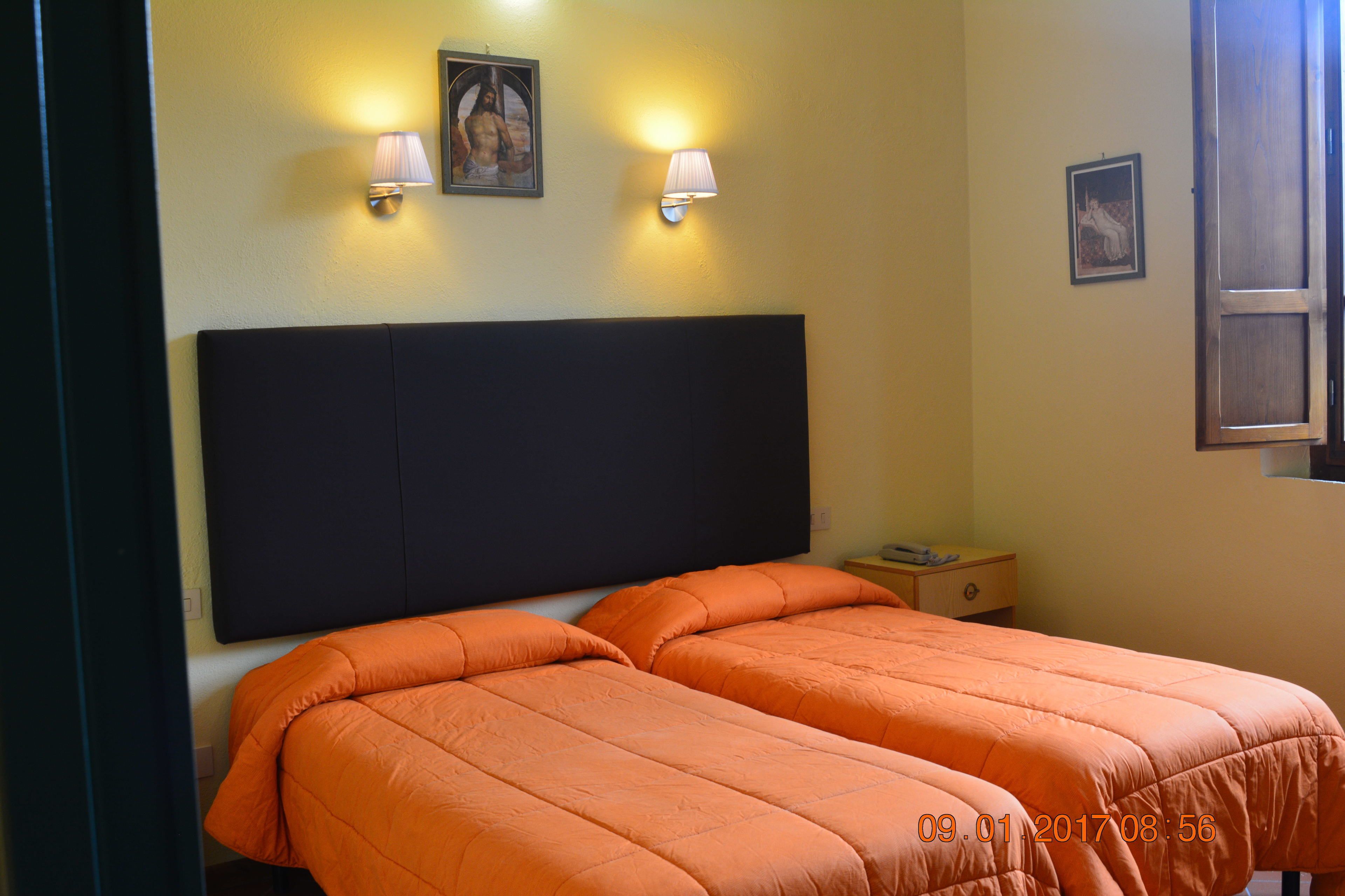 A hotel room with two beds, a nightstand, and two wall-mounted lamps.