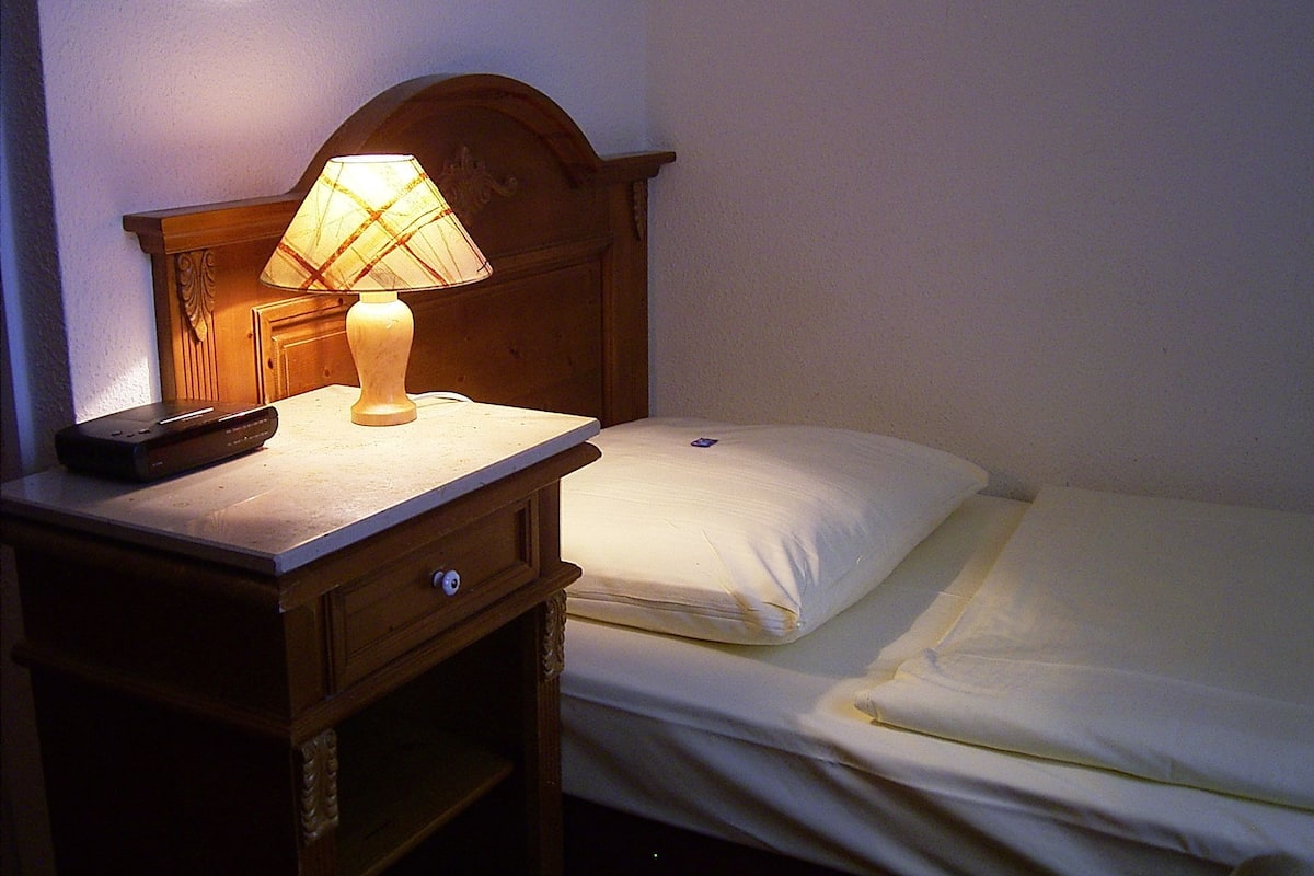 Une chambre d’hôtel avec une table de chevet en bois, une lampe, une télécommande et un lit parfaitement fait.