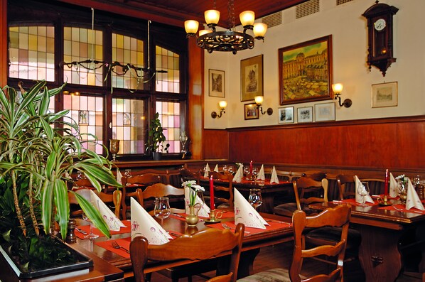Un comedor con mesas y sillas de madera, y una araña.