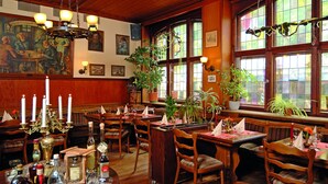 A restaurant interior with wooden furniture, multiple tables, potted plants, and a chandelier. - Hotel Restaurant Bockshaut (Darmstadt)