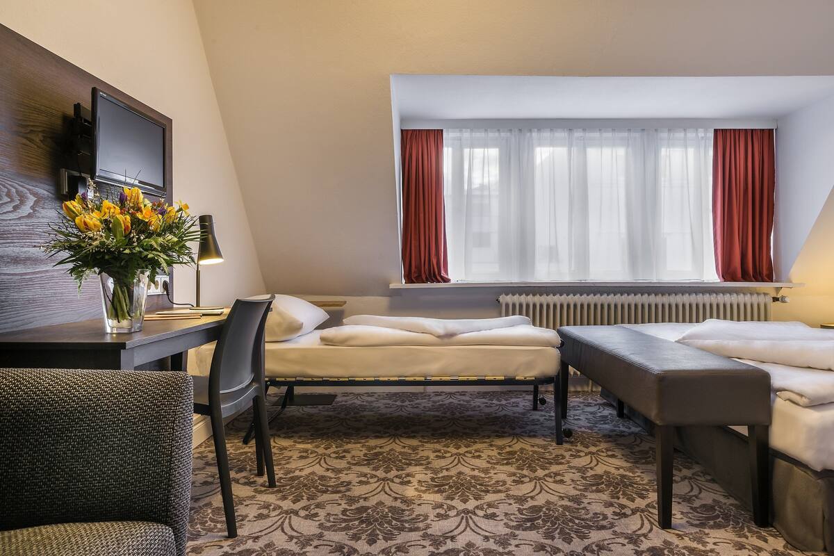 Een hotelkamer met een bed, een bureau met lamp, een stoel en een raam met gordijnen.