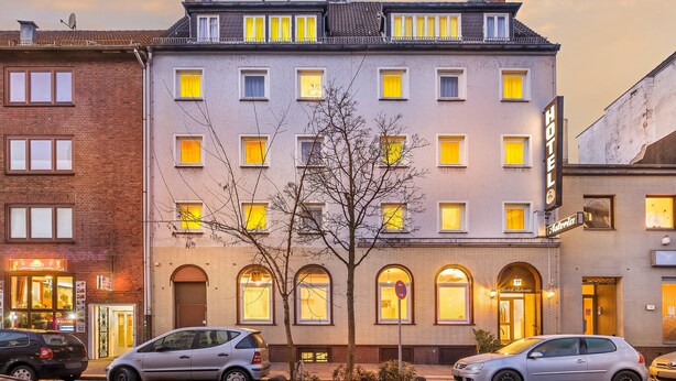 Een hotel met meerdere ramen, een boom ervoor en geparkeerde auto's.