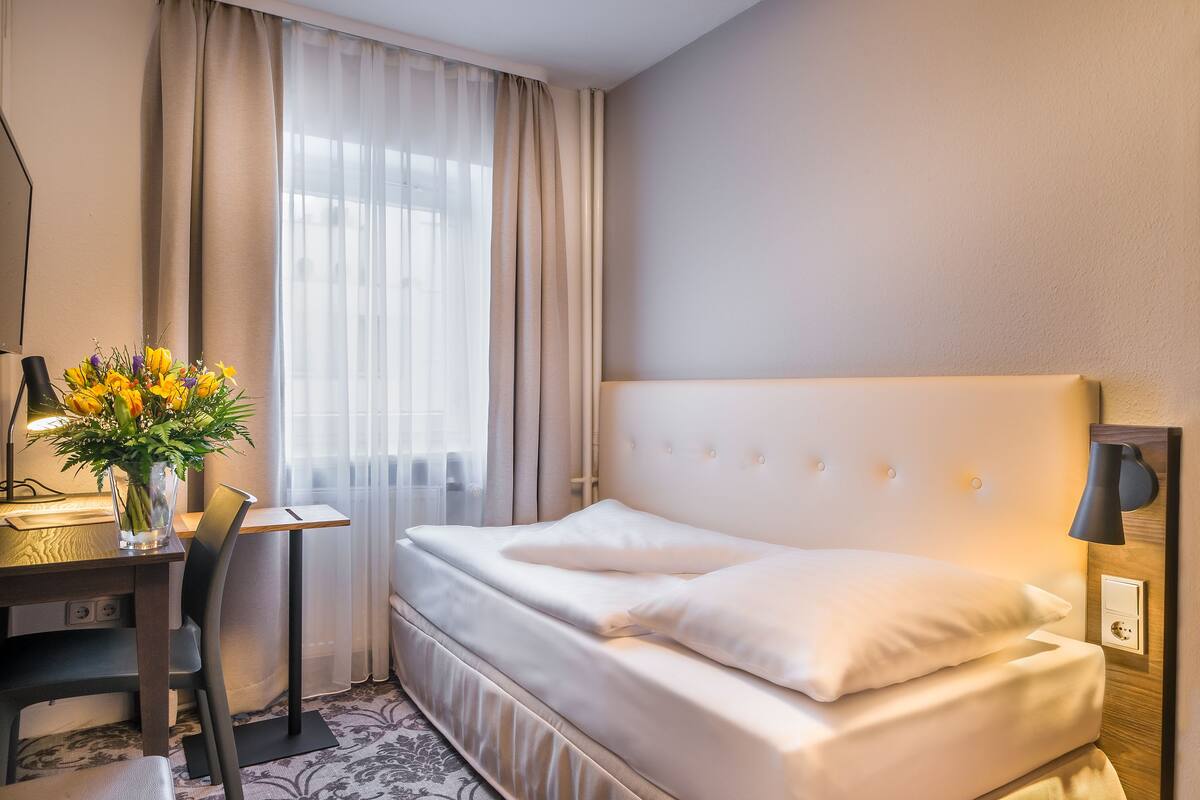 Een hotelkamer met een bed, een bureau, een stoel, een lamp en een bloemenvaas.