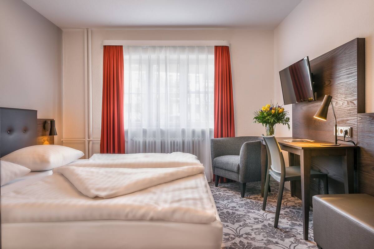 Een hotelkamer met een bed, een bureau, een stoel, een televisie en een raam met gordijnen.