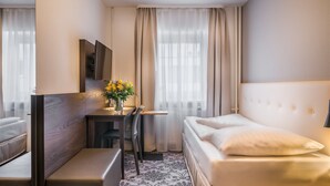 Een hotelkamer met een bed, een bureau, een stoel, een kleine tafel met een bloevas en een televisie aan de muur.