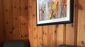 Une pièce aux murs lambrés, avec une table ronde en bois, deux chaises à motifs et un tableau encadré.