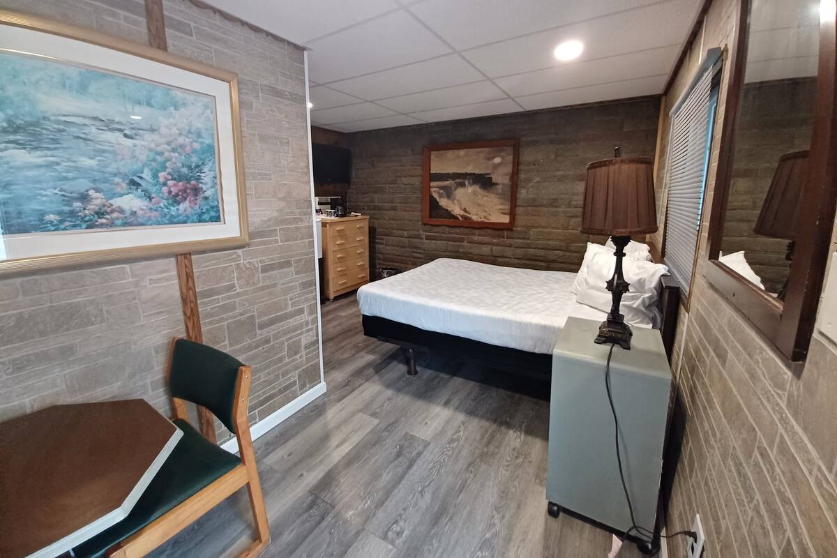 Une chambre à coucher comprenant un lit, un bureau, une chaise, une commode, une lampe et deux tableaux accrochés aux murs.