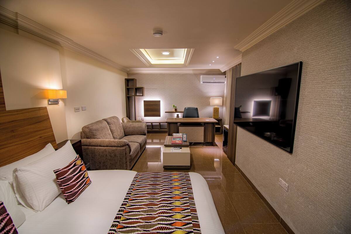 A hotel room with a bed, a sofa, a desk, and a TV.
