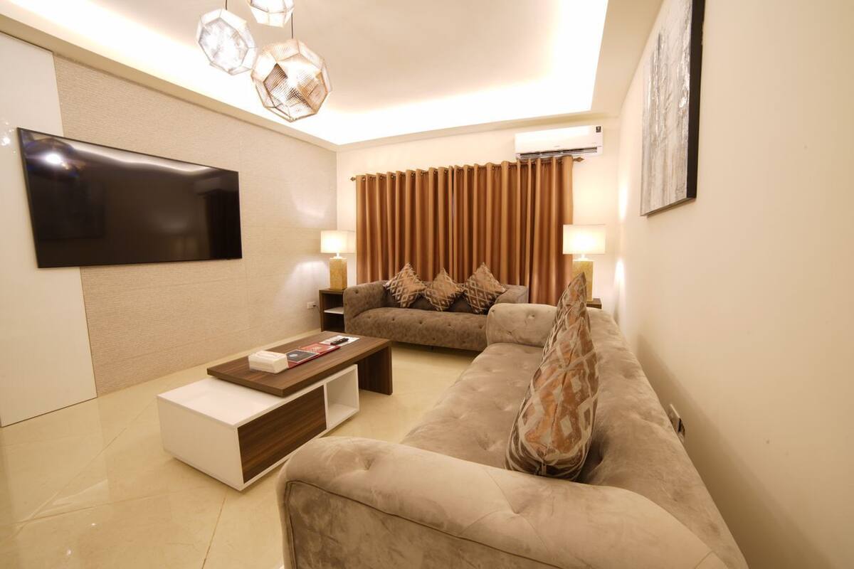 A modern living room with a flat-screen TV, a sofa, a coffee table, and a patterned throw pillow.