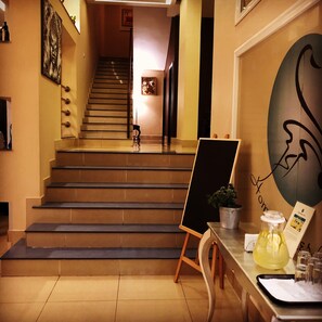 A staircase leading to a higher floor, a painting on the wall, and a table with a plant and a glass pitcher.