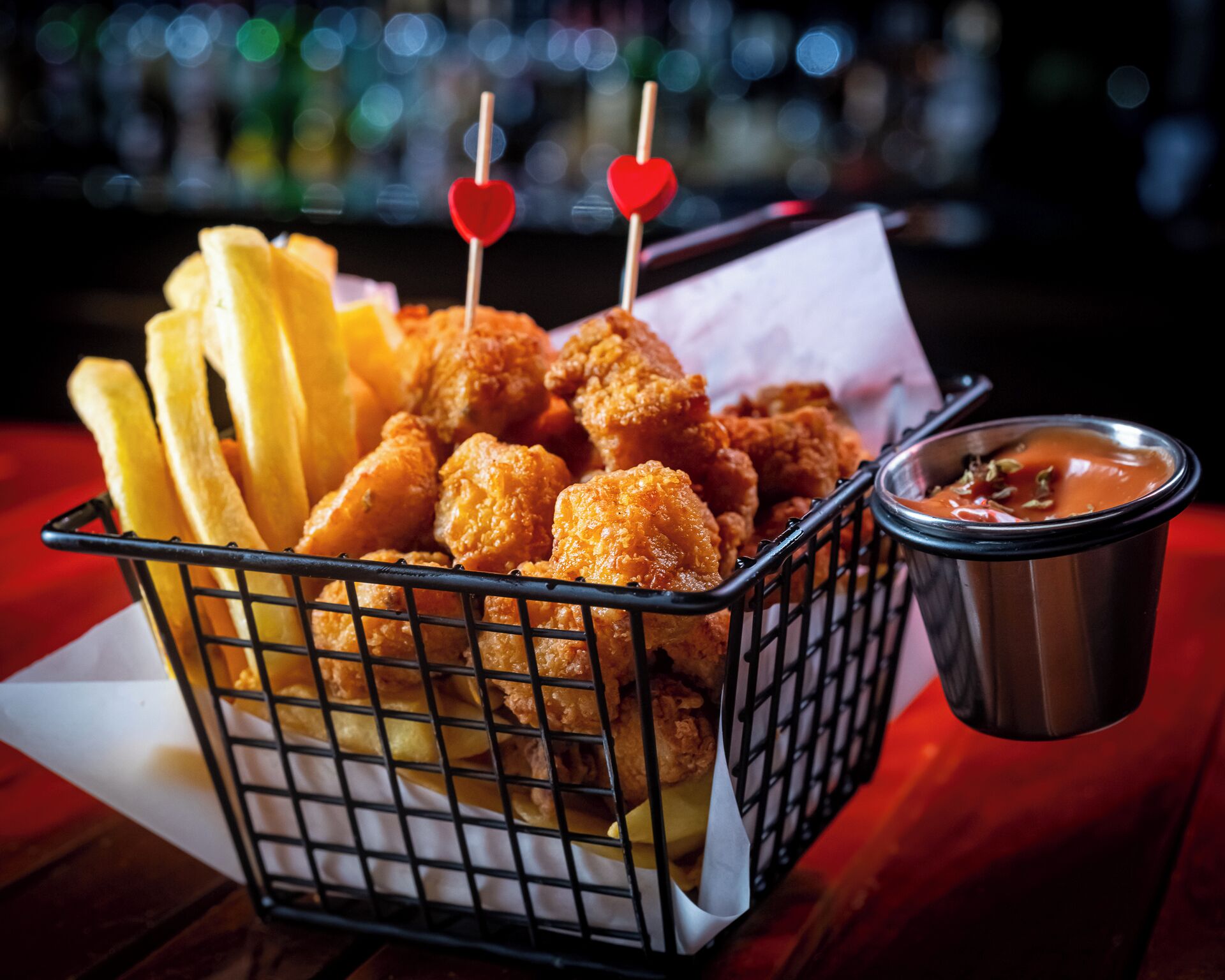 Een mand met gefrituurde kippennuggets en frietjes met saus.