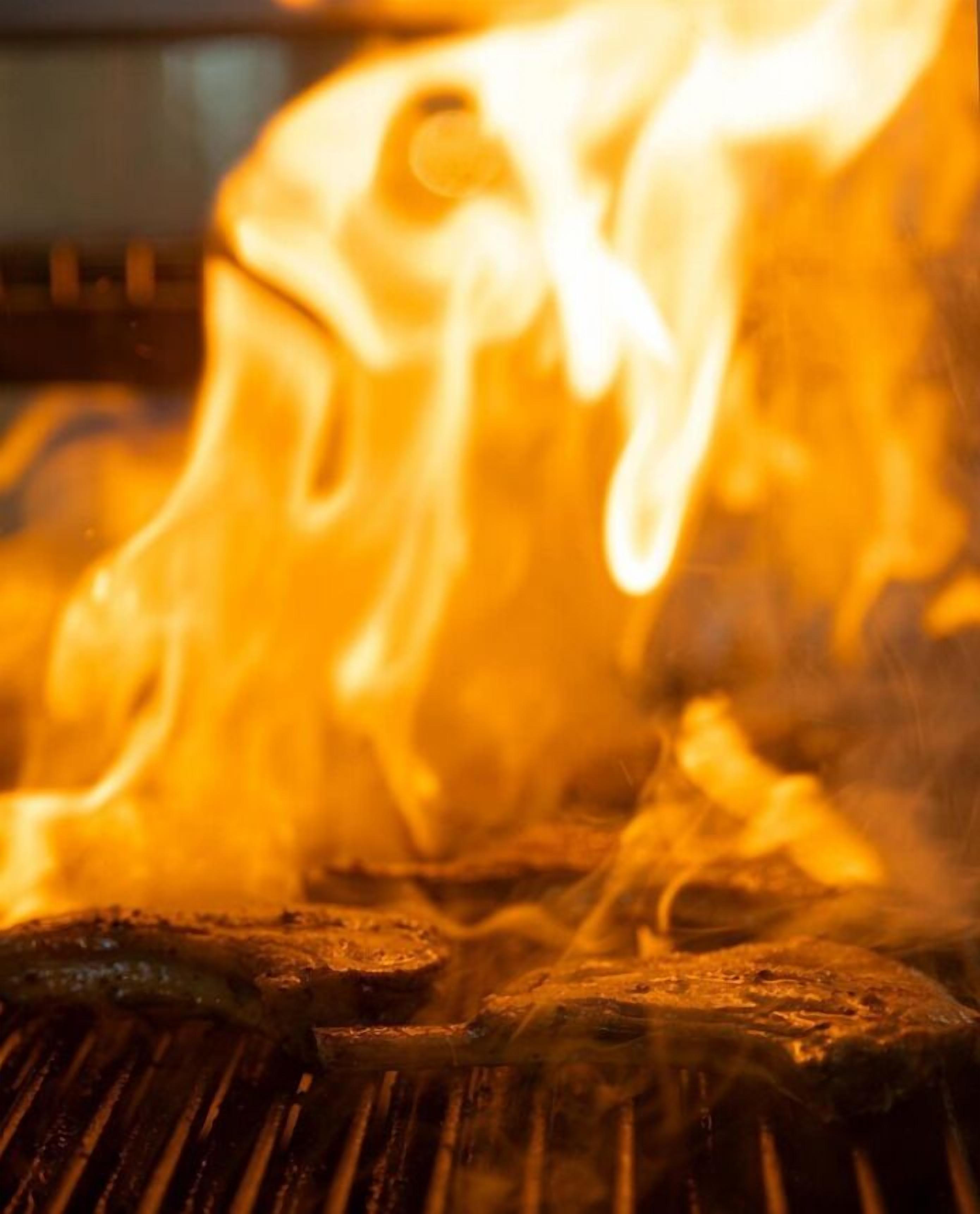Een grill met zichtbare vlammen en rook, wat aangeeft dat er wordt gekookt.