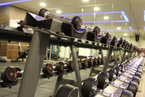 Un gimnasio con filas de mancuernas sobre estantes.