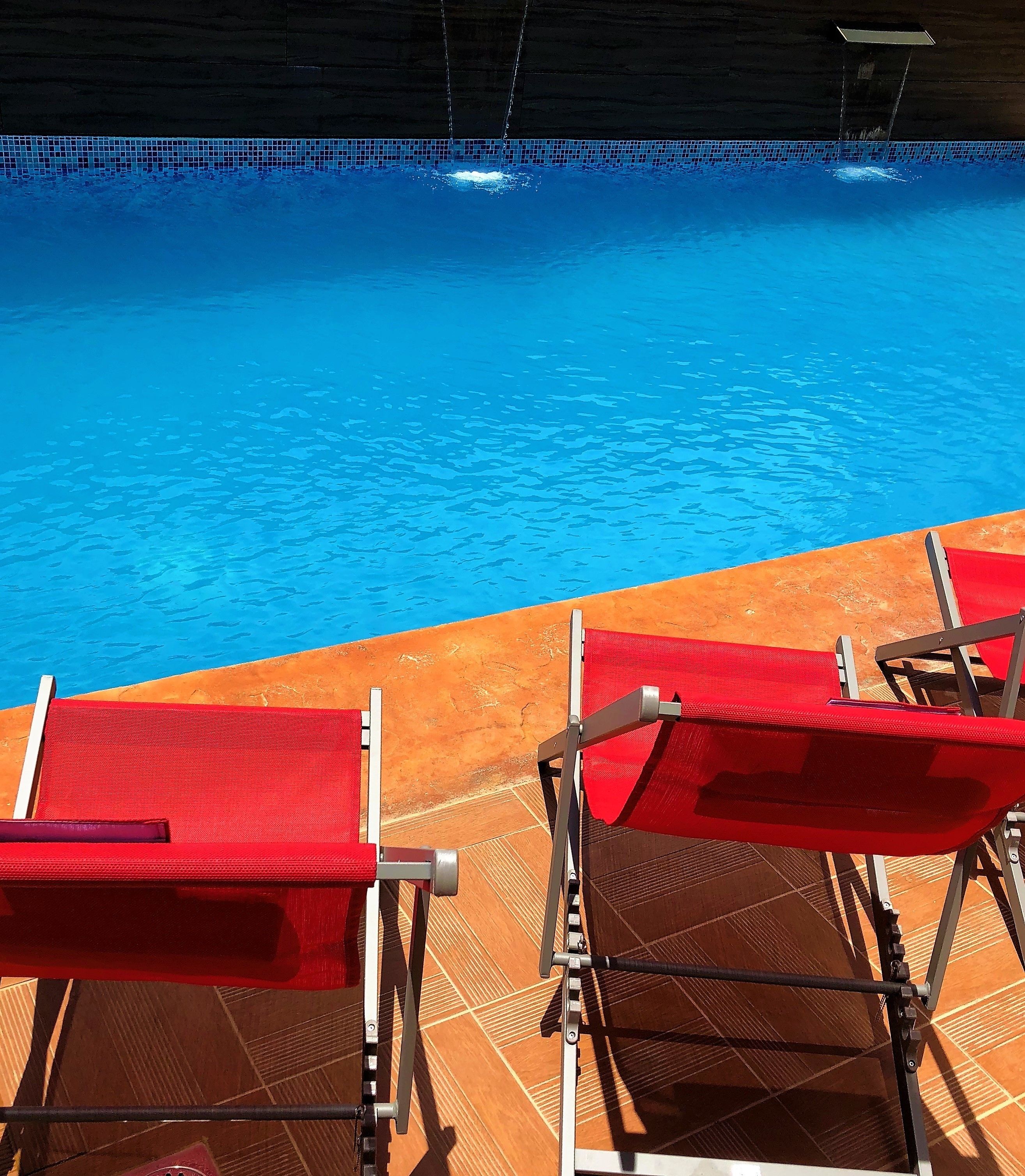 A poolside area with red lounge chairs and a tiled floor.