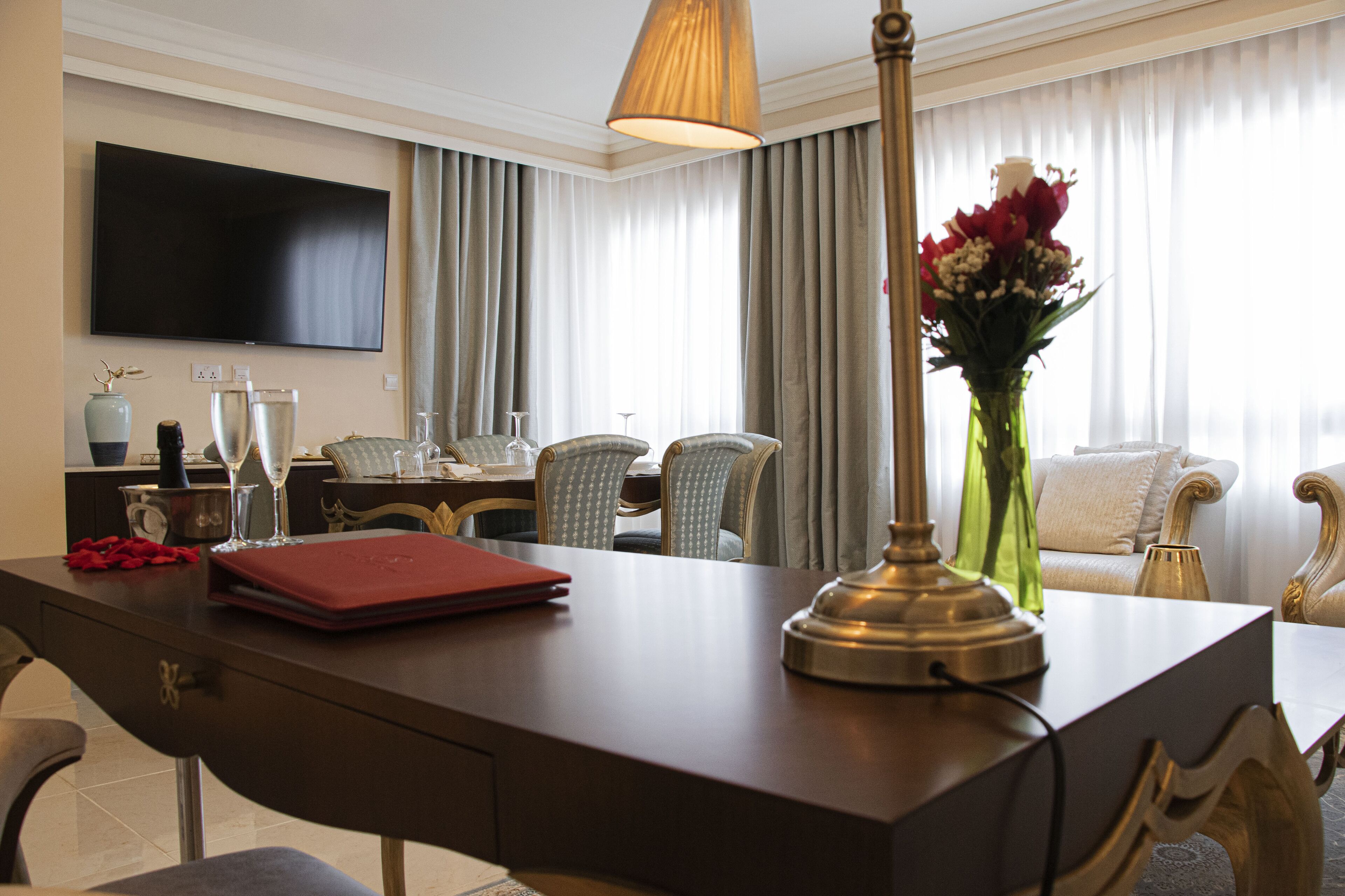 Ein Hotelzimmer mit Schreibtisch, Flachbildfernseher, Essbereich mit Stühlen, einer Blumenvase und einer Couch.