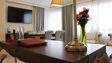Ein Hotelzimmer mit Schreibtisch, Flachbildfernseher, Essbereich mit Stühlen, einer Blumenvase und einer Couch.