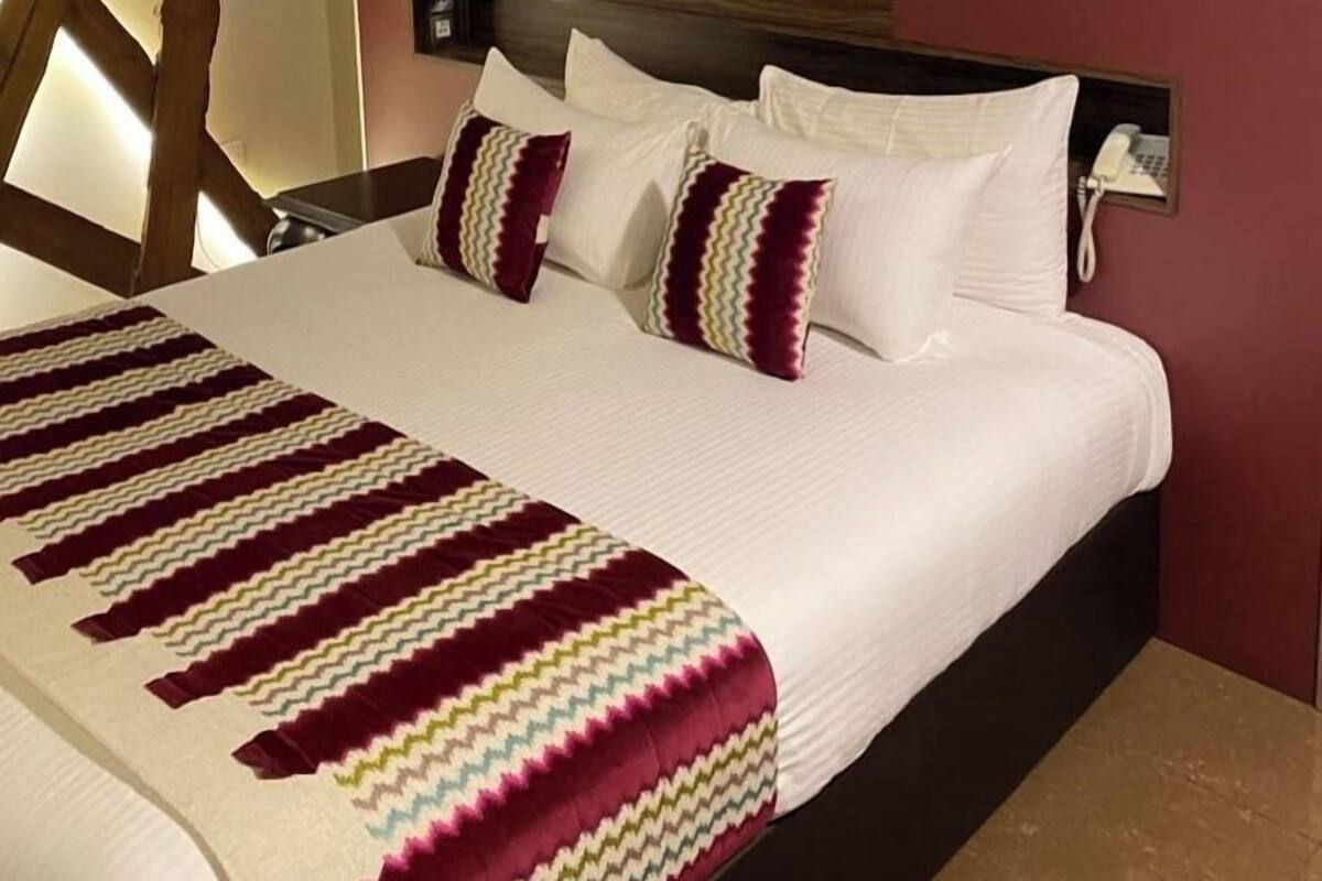 A hotel room with a large bed, white bedding, and a striped throw blanket.