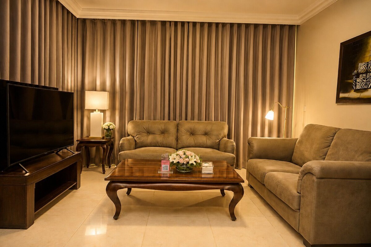 Una sala de estar con televisor, dos sofás, una mesa de centro con flores y una lámpara.