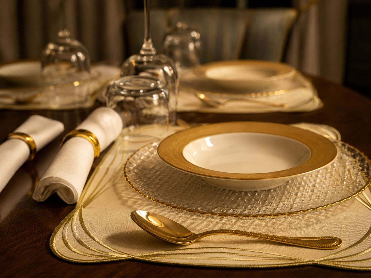 A table set with a gold-rimmed plate, a folded napkin, and a gold spoon.