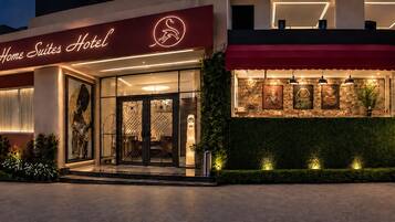The exterior of a hotel with a neon sign, a glass entrance, and a landscaped garden.