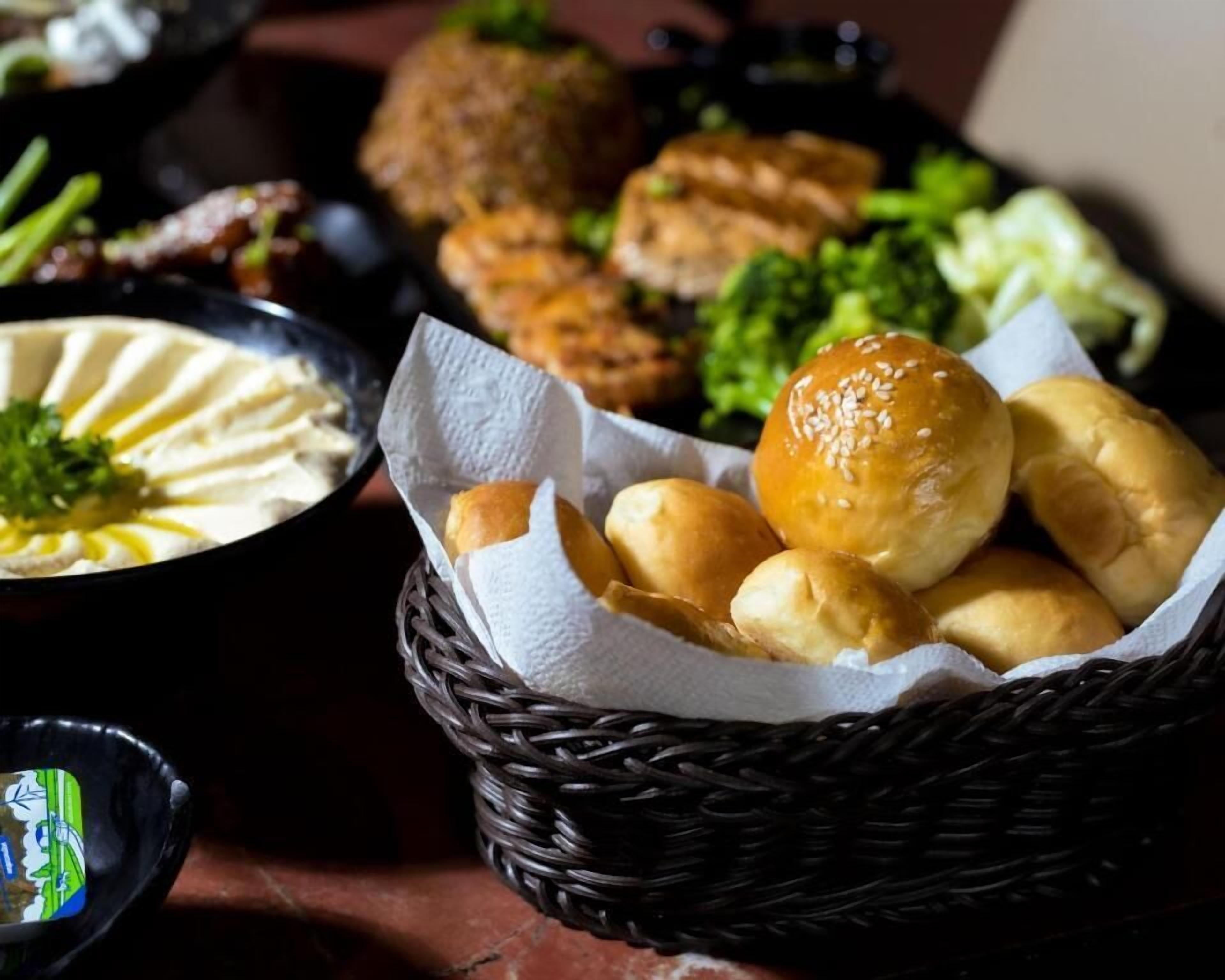 A basket of bread rolls on a table with various dishes in the background.