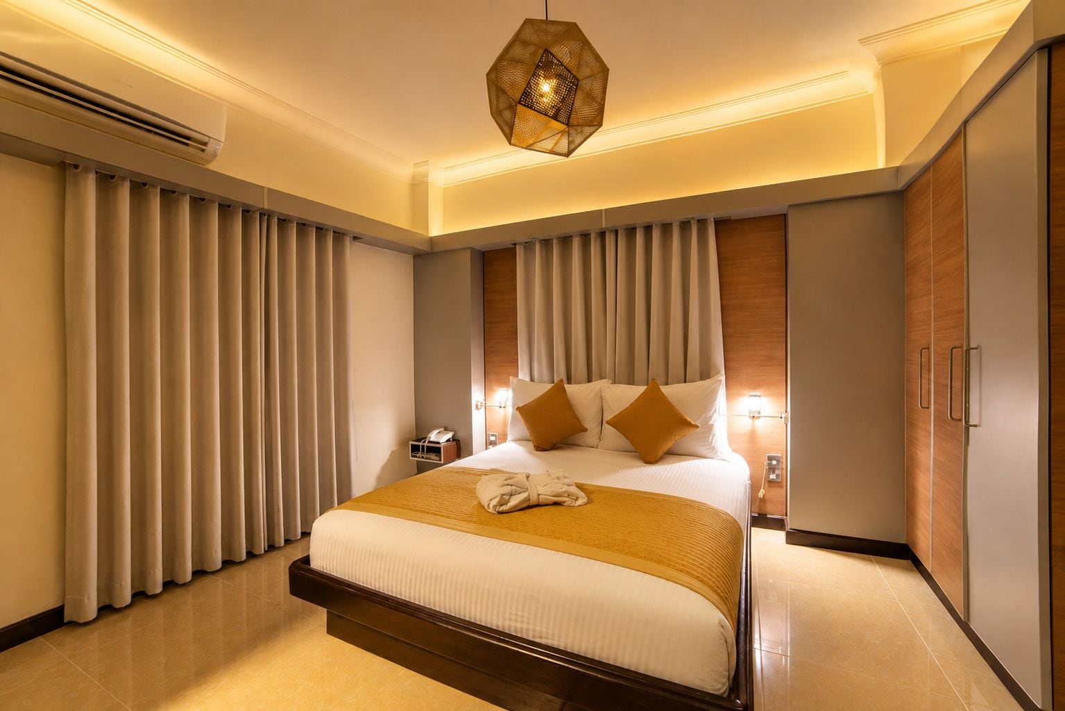 Une chambre d’hôtel avec un grand lit, des rideaux, un luminaire suspendu et une armoire.