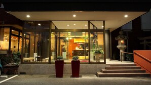 Entrada de hotel con fachada de vidrio, un mostrador de recepción y una escalera que lleva al vestíbulo.