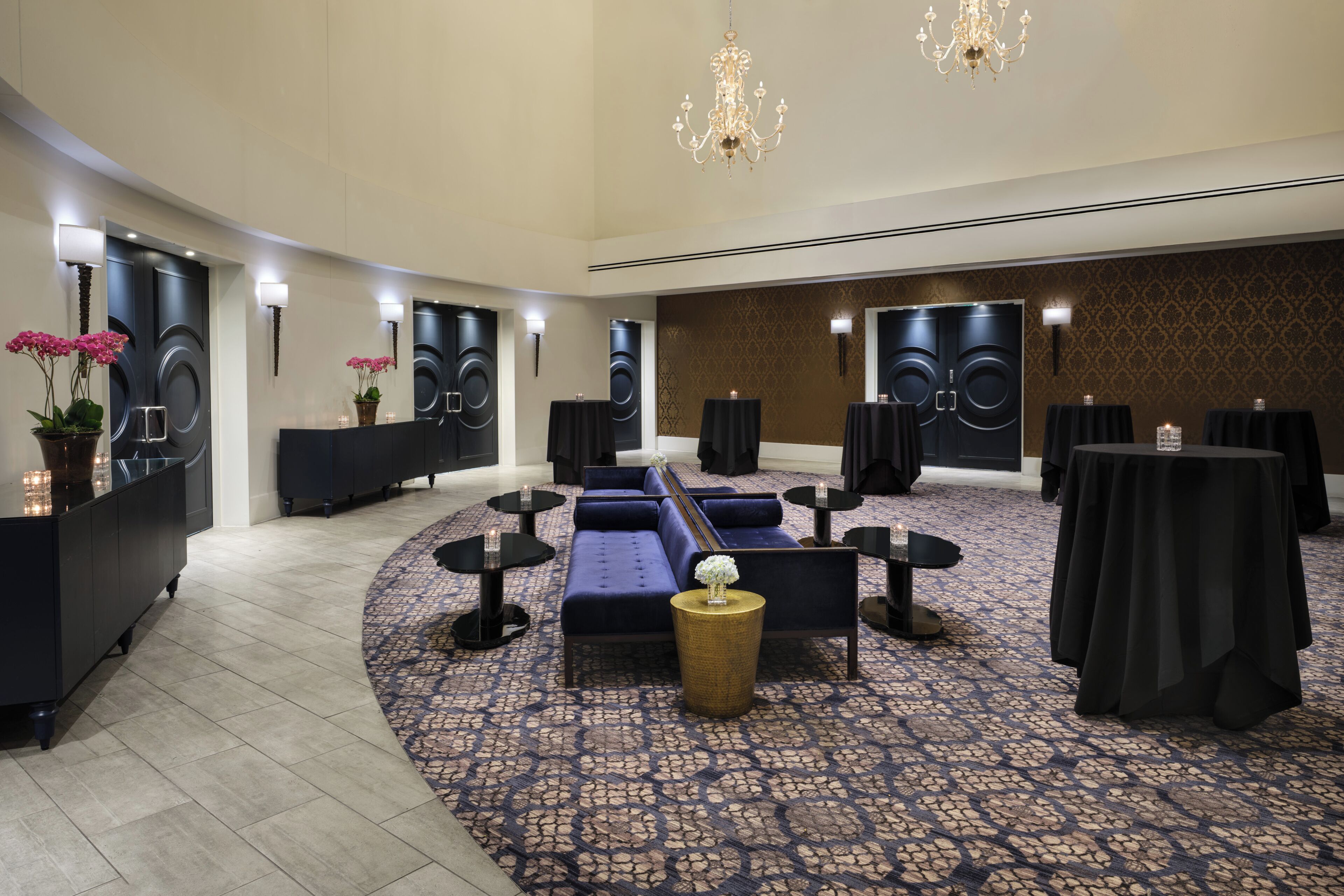 A hotel lobby with a curved seating area, black tables, and a patterned carpet.